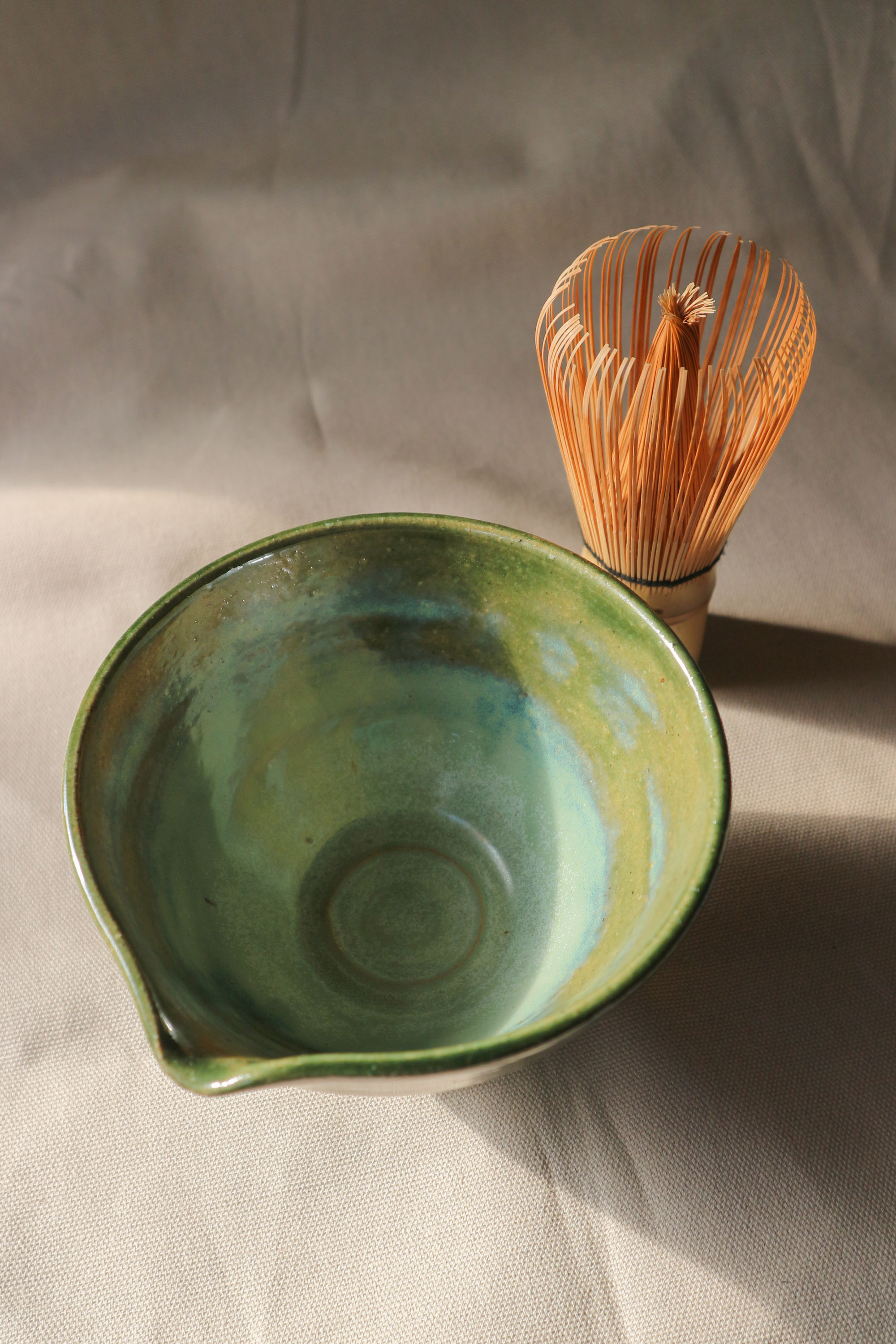 Hand-thrown stoneware ceramic matcha bowl by Eden Hoang. The bowl is glazed in a deep forest green, with a matcha whisk sitting beside the bowl.